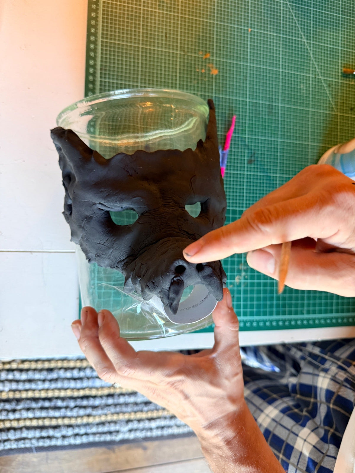 Front view of a black foam clay werewolf mask as a finger smooths the nose